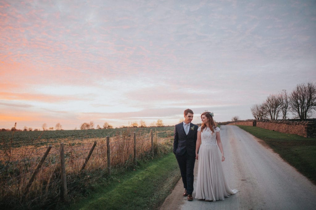 bride and groom walking through the cotswolds at sunset 