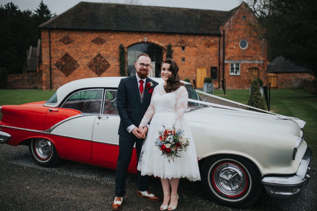 bride and groom with retro American wedding car in front of Shustoke Farm Barn 