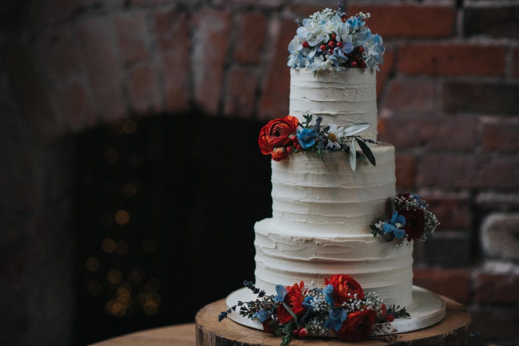 vintage wedding cake with red and blue flowers at Shustoke Farm Barns.