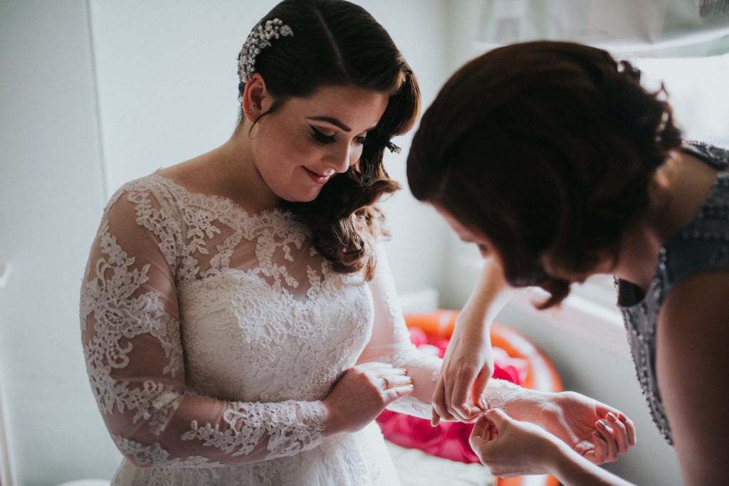 Vintage glamour bride getting dressed into her wedding dress by her bridesmaid. 
