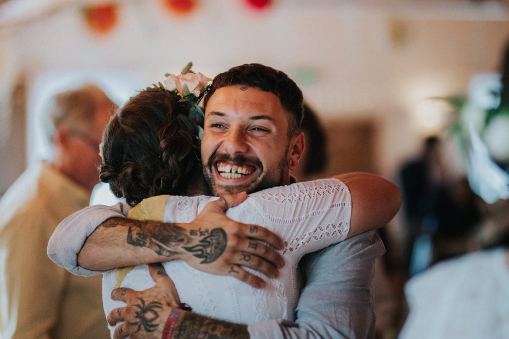 tattooed wedding guest hugging bride at Maxstoke Village Hall wedding.