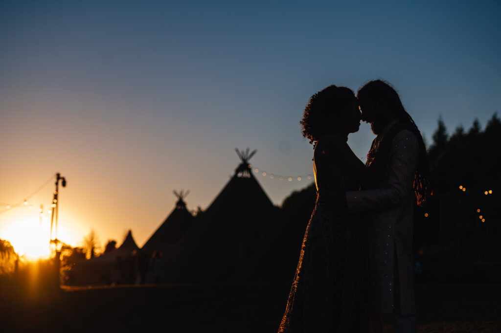 silhouette of bride and groom at sunset infront of tipis at Hadham Farm